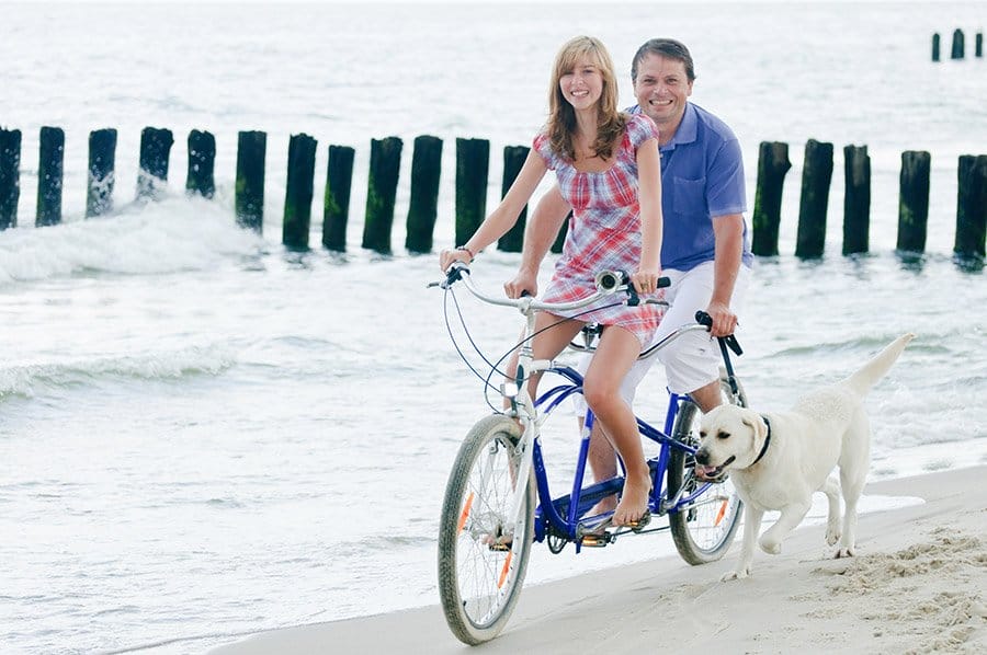 man en vrouw fietsen met hond op strand